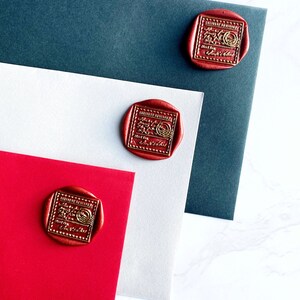 Puede incluir: Sellos de cera rojos con letras doradas est&aacute;n adheridos a sobres rojos, blancos y azul oscuro. Los sellos tienen un dise&ntilde;o rectangular con las palabras "DELIVERY CONFIRMED" y otro texto. Los sobres est&aacute;n dispuestos sobre una superficie de m&aacute;rmol blanco.