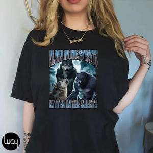May include: Black t-shirt featuring a graphic of three wolves howling at the moon. The text "Alpha in the Streets Kitten in the Sheets" is printed on the shirt.