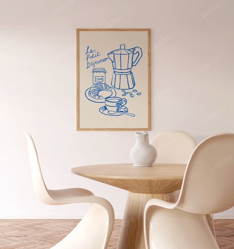 May include: A blue line drawing of a coffee pot, a cup of coffee, a croissant, and a jar of jam on a cream background. The text "Le Petit D&eacute;jeuner" is written in blue above the drawing. The drawing is framed in a light wood frame.