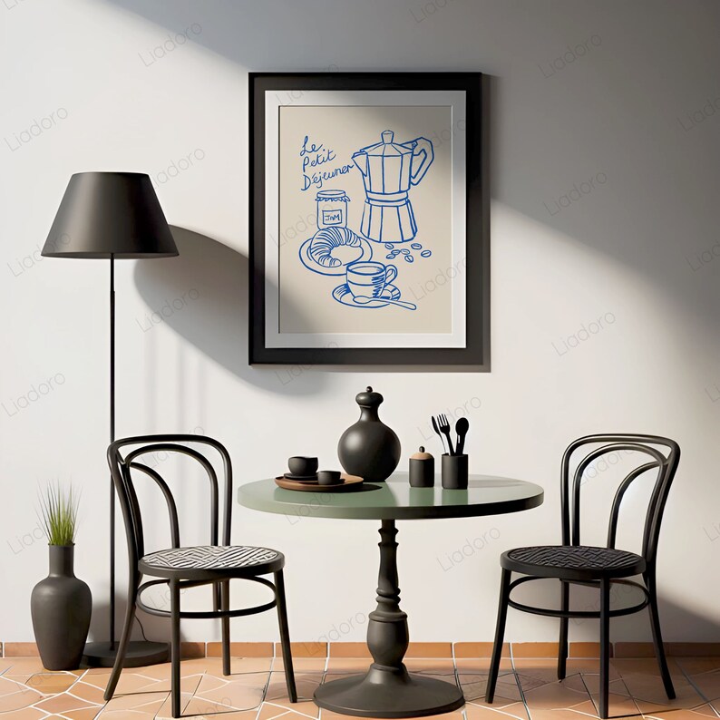 May include: A black framed illustration of a French breakfast scene with a coffee pot, a croissant, a cup of coffee, and the text "Le Petit Dejeuner". The illustration is on a beige background. The illustration is hanging on a white wall above a black round table with two black chairs. There is a black floor lamp with a black lampshade in the corner of the room.