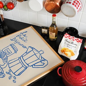 May include: A framed illustration of a coffee pot, coffee beans, and a jar of jam with the text "Le Petit D&eacute;jeuner" in blue lettering on a beige background.