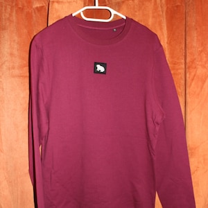 May include: A maroon long-sleeved sweatshirt with a small white logo of a sitting animal on the front.