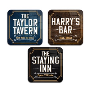 May include: Three square-shaped signs with gold frames and vintage-style lettering. The first sign is blue with white text that reads "The Taylor Tavern Est. 2022 by Clive". The second sign is brown with white text that reads "Harry's Bar Est. 2022". The third sign is black with white text that reads "The Staying Inn Open Till Late".