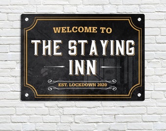 May include: Black metal sign with gold trim and text that reads "Welcome to The Staying Inn - Est. Lockdown 2020".