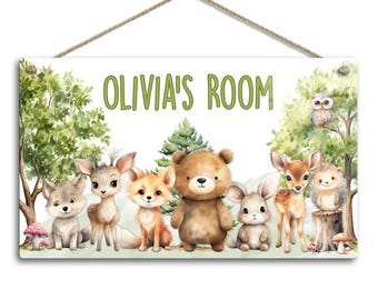 May include: A white wooden sign with the text "Olivia's Room" in green lettering. The sign is decorated with watercolour illustrations of woodland animals, including a fox, a deer, a bear, a rabbit, a wolf, and a hedgehog. The animals are surrounded by green leaves and a mushroom.