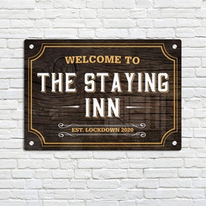 Könnte beinhalten: Ein rustikales Holzschild mit goldener Umrandung und dem Text "Willkommen im The Staying Inn - Est. Lockdown 2020".