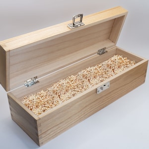 May include: A wooden box with a hinged lid and a metal latch. The box is filled with shredded paper, which is commonly used for packaging fragile items.