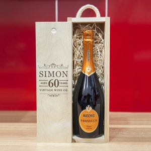 Puede incluir: Una botella de Maschio Prosecco en una caja de regalo de madera. La botella tiene una tapa de lámina dorada y una etiqueta con las palabras "Maschio Prosecco". La caja de madera está grabada con las palabras "SIMON AGED 60 YEARS VINTAGE WINE CO."