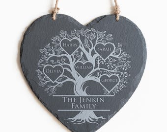 May include: Heart-shaped slate sign with a family tree design. The tree has heart-shaped leaves with names: Olivia, Harry, William, Sarah, and George. The text "THE JENKIN FAMILY" is at the bottom. A jute rope is attached for hanging.