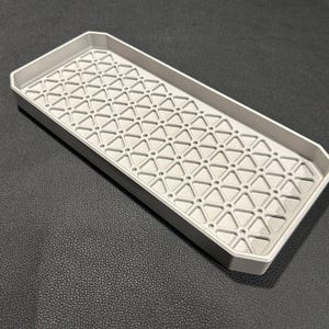 May include: A gray rectangular tray with a geometric pattern of small triangles. The tray has a raised edge around the perimeter.