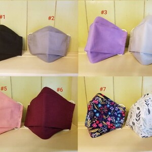 K&ouml;nnte beinhalten: Acht verschiedene Stoffmasken, nummeriert von 1 bis 8. Die Masken sind in verschiedenen Farben und Mustern, darunter Schwarz, Grau, Lila, Rosa, Burgunderrot, Blumenmuster und Wei&szlig; mit grauen Bl&auml;ttern.