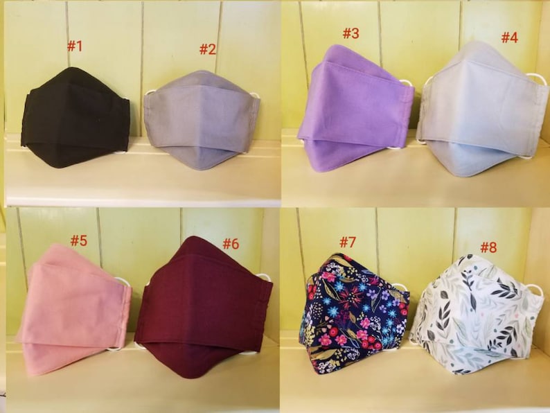 K&ouml;nnte beinhalten: Acht verschiedene Stoffmasken, nummeriert von 1 bis 8. Die Masken sind in verschiedenen Farben und Mustern, darunter Schwarz, Grau, Lila, Rosa, Burgunderrot, Blumenmuster und Wei&szlig; mit grauen Bl&auml;ttern.