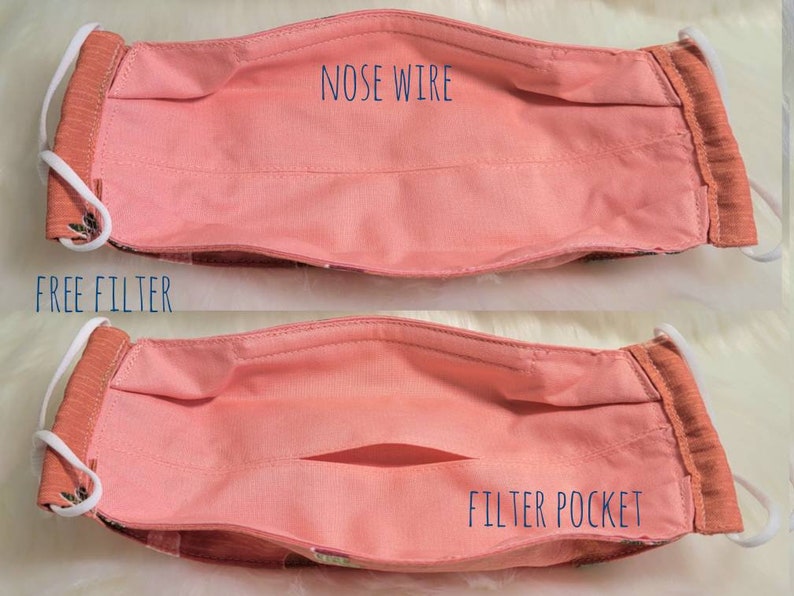 K&ouml;nnte beinhalten: Eine rosa Stoffmaske mit einem Fach f&uuml;r einen Filter und einem Nasendraht. Der Text "FREE FILTER" und "FILTER POCKET" ist auf der Maske aufgedruckt.