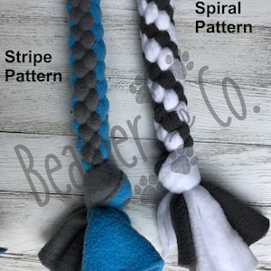 May include: Two dog toys with braided rope designs. One is blue and gray with "Stripe Pattern" text, and the other is white, gray, and black with "Spiral Pattern" text. Both have fleece tassels at the ends.