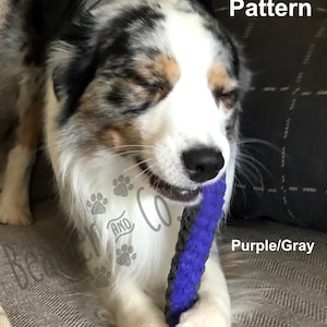 May include: A dog with a black, white, and gray coat is holding a purple and gray dog toy in its mouth. The toy has a small stripe pattern. Text on the image reads "Small Stripe Pattern" and "Purple/Gray".