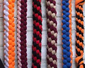 Könnte beinhalten: Sechs geflochtene Fleece-Seilspielzeuge für Haustiere, jedes mit einer einzigartigen Farbkombination aus Orange und Weiß, Kastanienbraun und Rosa, Rot und Schwarz, Beige und Kastanienbraun, Blau und Orange sowie Schwarz und Orange, mit verknoteten Enden.