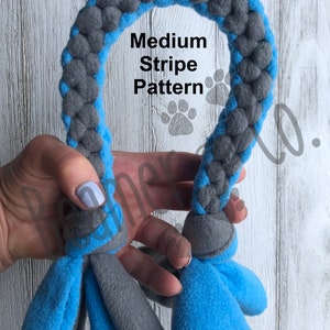 May include: Sky blue and gray dog toy with a braided rope design. The toy features a medium stripe pattern and fleece tassels at both ends. The text "Medium Stripe Pattern" and "Sky Blue/Gray" are visible.