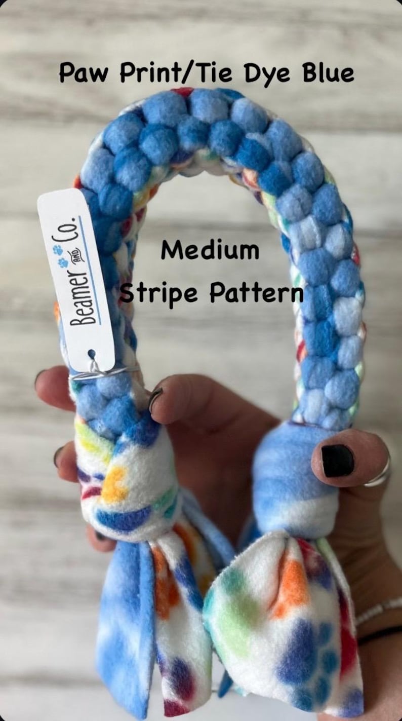 May include: A blue and white dog toy with a medium stripe pattern. The toy is made of soft fabric and has a tie-dye design with blue, orange, and yellow accents. The tag reads "Beamer & Co."