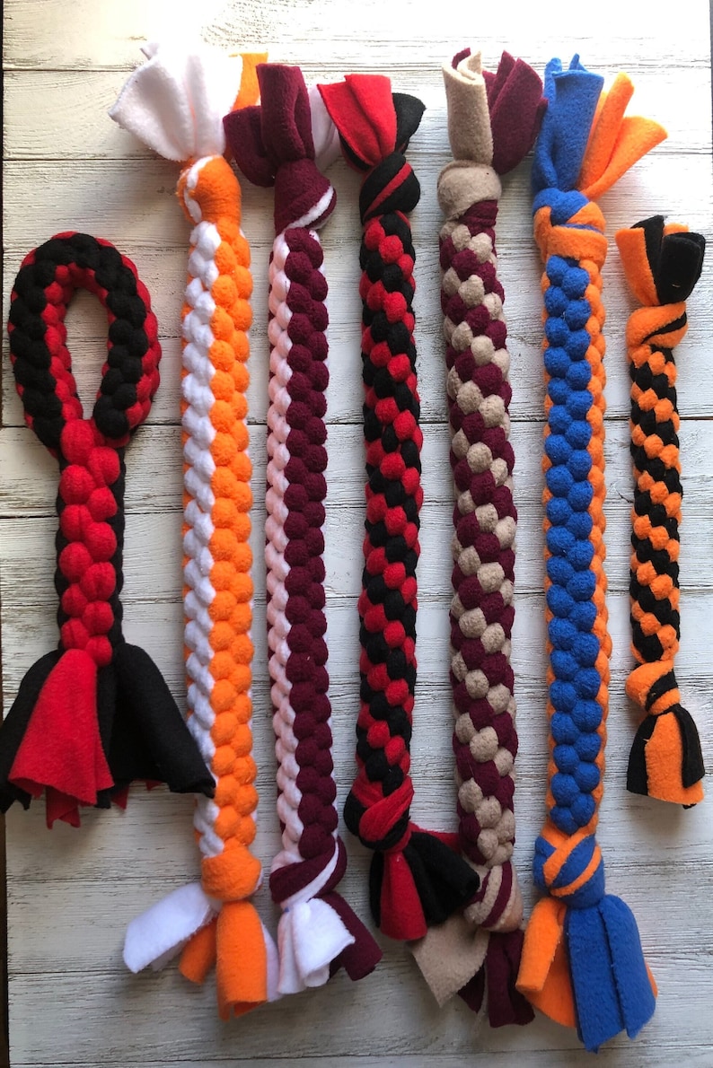 May include: A collection of colorful dog toys made from braided fleece. The toys feature various color combinations, including red, black, orange, white, pink, and blue. Each toy has knotted ends for added durability and play.