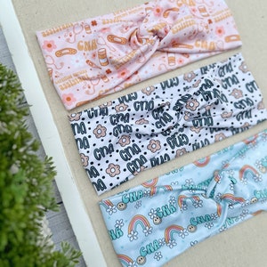 May include: Three colorful headbands with different patterns. The first headband is pink with a white background and features a repeating pattern of medical symbols, including a stethoscope, bandages, pills, and the text "Certified Nursing Assistant" and "CNA". The second headband is white with a black background and features a repeating pattern of black dots, white flowers, and the text "CNA". The third headband is light blue with a white background and features a repeating pattern of rainbows, white flowers, and the text "CNA".