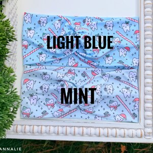 May include: Two light blue and mint headbands with a repeating pattern of cartoon teeth wearing Santa hats and holding toothbrushes and candy canes. The text "LIGHT BLUE" and "MINT" are printed on the headbands.