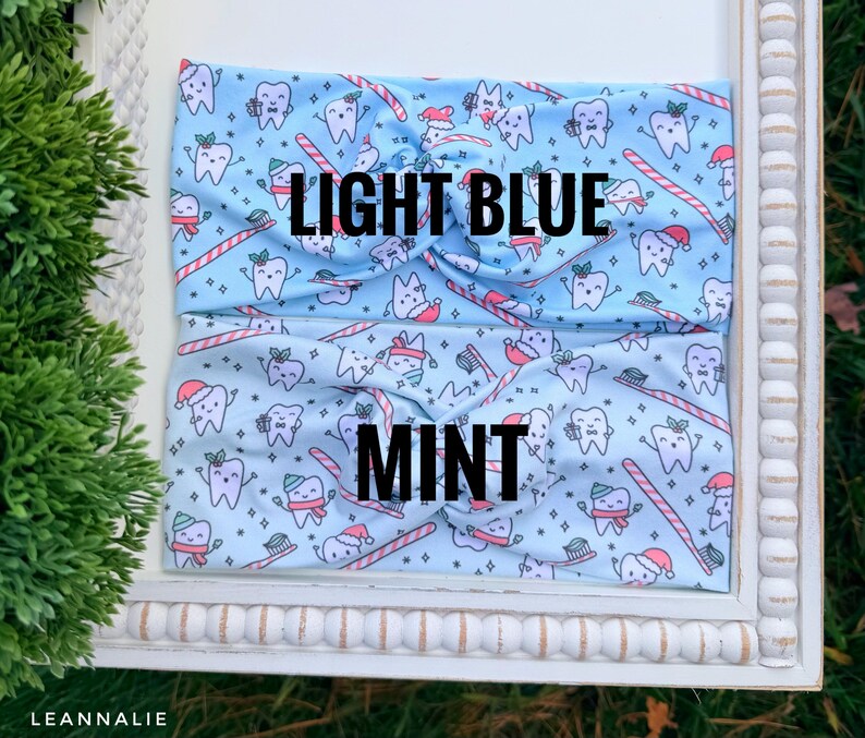 May include: Two light blue and mint headbands with a repeating pattern of cartoon teeth wearing Santa hats and holding toothbrushes and candy canes. The text "LIGHT BLUE" and "MINT" are printed on the headbands.