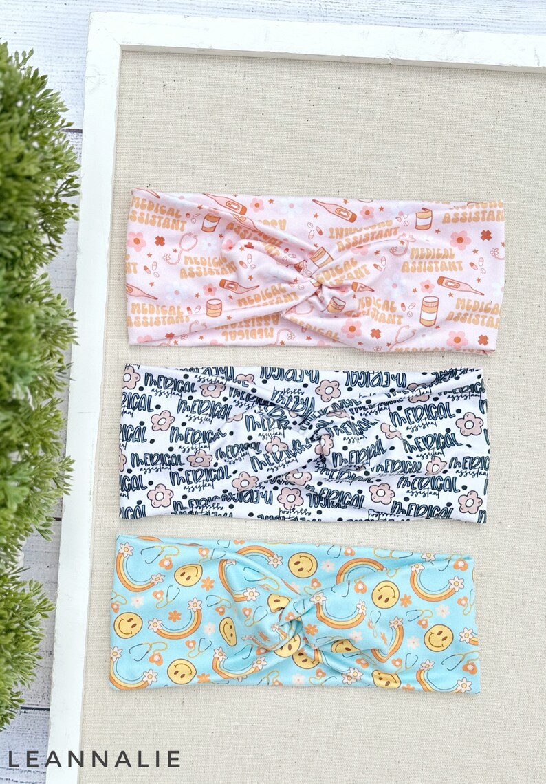 May include: Three different patterned headbands. The top headband is pink with a white pattern of medical symbols and the text "Medical Assistant". The middle headband is white with a black pattern of flowers and the text "Medical". The bottom headband is light blue with a pattern of rainbows, smiley faces, and stethoscopes.