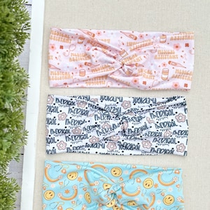 May include: Three different patterned headbands. The top headband is pink with a white pattern of medical symbols and the text "Medical Assistant". The middle headband is white with a black pattern of flowers and the text "Medical". The bottom headband is light blue with a pattern of rainbows, smiley faces, and stethoscopes.