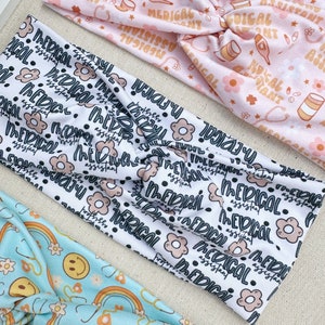 May include: Three different patterned headbands. The first headband is pink with a white background and features a repeating pattern of medical symbols and the text "Medical Assistant". The second headband is white with a black background and features a repeating pattern of black dots, pink flowers, and the text "Medical Assistant". The third headband is light blue with a white background and features a repeating pattern of rainbows, yellow smiley faces, and white flowers.