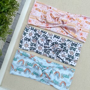 May include: Three colorful headbands with different patterns. The top headband is pink with a white pattern of medical symbols, the middle headband is white with a black and brown pattern of flowers and the text "CNA", and the bottom headband is light blue with a white pattern of rainbows and the text "CNA".