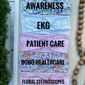 K&ouml;nnte beinhalten: F&uuml;nf bunte Stirnb&auml;nder mit verschiedenen Designs. Das obere Stirnband hat einen wei&szlig;en Hintergrund mit rosa, blauen und gr&uuml;nen Schleifendesigns und die Worte "AWARENESS" in Schwarz. Das zweite Stirnband hat einen wei&szlig;en Hintergrund mit einem hellblauen EKG-Muster. Das dritte Stirnband hat einen rosa Hintergrund mit einem wei&szlig;en Patientenpflege-Design. Das vierte Stirnband hat einen wei&szlig;en Hintergrund mit einem rosa und gelben Blumendesign und die Worte "BOHO HEALTHCARE" in Schwarz. Das f&uuml;nfte Stirnband hat einen rosa Hintergrund mit einem wei&szlig;en Blumendesign und die Worte "FLORAL STETHOSCOPES" in Schwarz.