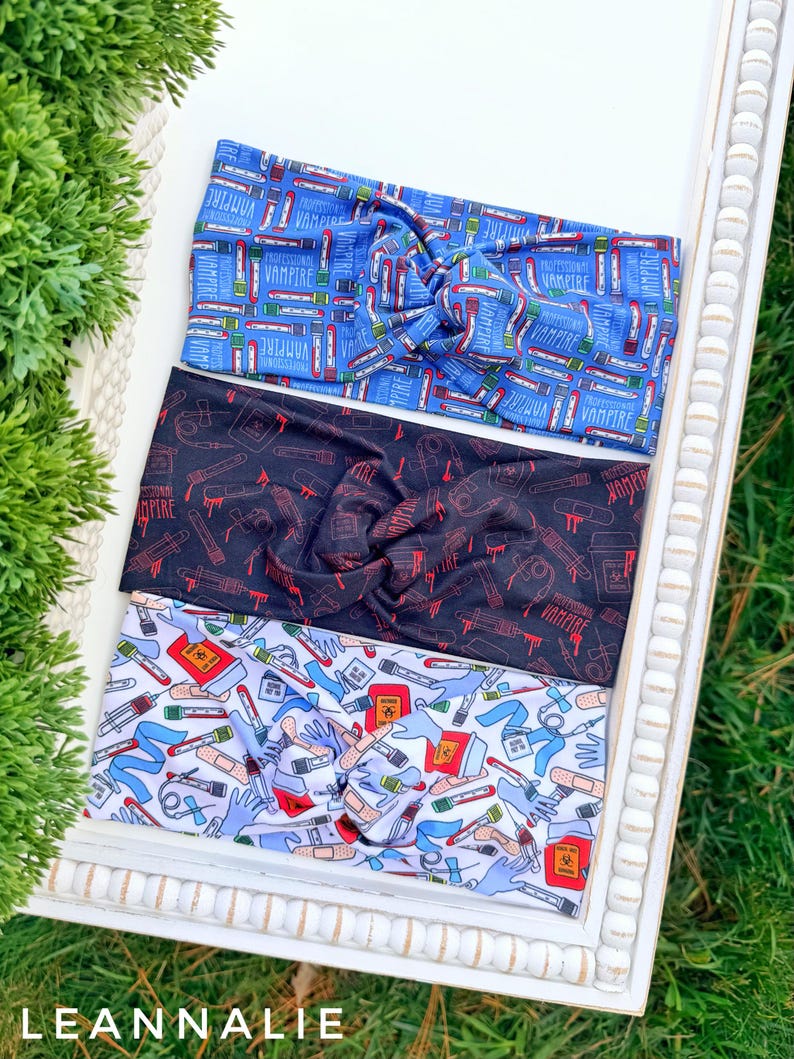 Op de afbeelding: Drie stoffen haarbanden met een gedraaid knoopontwerp. De bovenste haarband is blauw met een patroon van vampier-thema-items. De middelste haarband is zwart met rode vampier-thema-items. De onderste haarband is wit met een medisch thema.