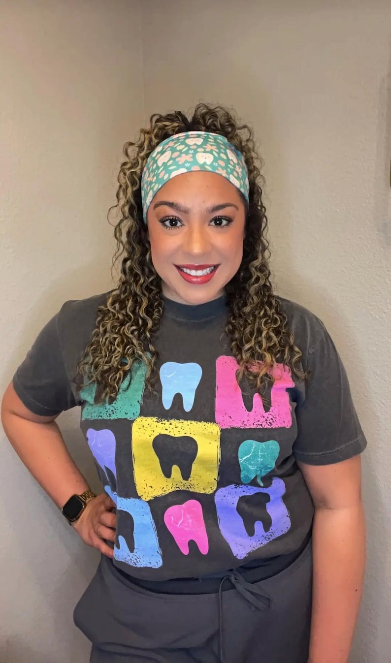 May include: A charcoal gray short-sleeve t-shirt featuring a grid of colorful, distressed-style squares, each containing a solid black tooth icon. The shirt is paired with a light blue headband decorated with a repeating pattern of small white teeth and flowers.