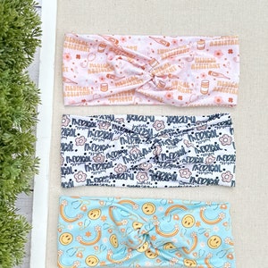 May include: Three different patterned headbands. The top headband is pink with a white pattern of medical assistant text, pills, and thermometers. The middle headband is white with a black pattern of flowers and the text "Medical". The bottom headband is light blue with a yellow pattern of smiley faces and rainbows.