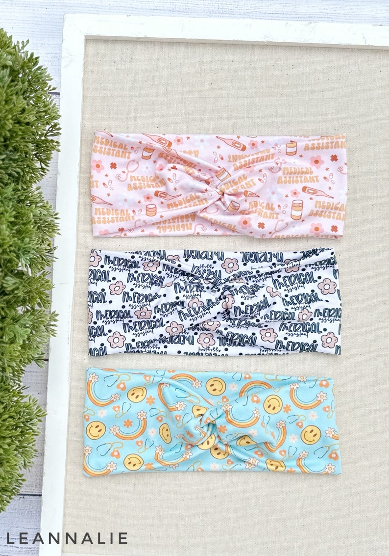 May include: Three different patterned headbands. The top headband is pink with a white pattern of medical assistant text, pills, and thermometers. The middle headband is white with a black pattern of flowers and the text "Medical". The bottom headband is light blue with a yellow pattern of smiley faces and rainbows.