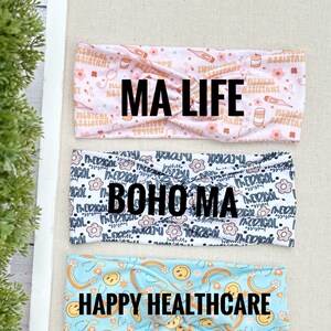 May include: Three colorful headbands with different patterns. The top headband is pink with a white pattern of medical symbols and the text "MA LIFE". The middle headband is white with a black pattern of flowers and the text "BOHO MA". The bottom headband is light blue with a yellow pattern of rainbows and smiley faces and the text "HAPPY HEALTHCARE".