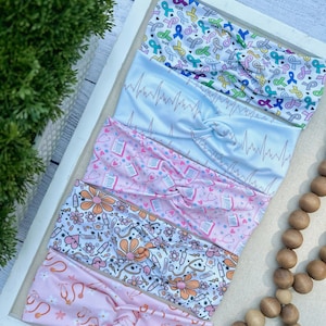 K&ouml;nnte beinhalten: F&uuml;nf verschiedene gemusterte Stirnb&auml;nder in verschiedenen Farben, darunter Rosa, Blau und Wei&szlig;. Die Stirnb&auml;nder zeigen Designs im Zusammenhang mit dem Gesundheitswesen, wie z. B. medizinische Symbole, B&auml;nder und EKG-Linien. Die Stirnb&auml;nder sind in einer Reihe auf einer wei&szlig;en Oberfl&auml;che angeordnet.