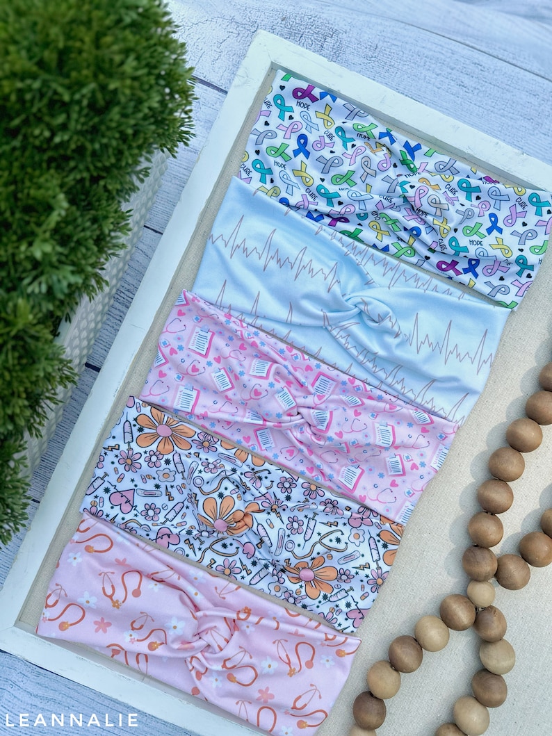 K&ouml;nnte beinhalten: F&uuml;nf verschiedene gemusterte Stirnb&auml;nder in verschiedenen Farben, darunter Rosa, Blau und Wei&szlig;. Die Stirnb&auml;nder zeigen Designs im Zusammenhang mit dem Gesundheitswesen, wie z. B. medizinische Symbole, B&auml;nder und EKG-Linien. Die Stirnb&auml;nder sind in einer Reihe auf einer wei&szlig;en Oberfl&auml;che angeordnet.
