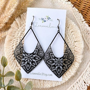 May include: A pair of black teardrop-shaped earrings featuring an intricate laser-cut floral mandala pattern. The earrings hang from dark metal hooks on a white display card printed with the text Leannalie and Leannalie.Etsy.com.