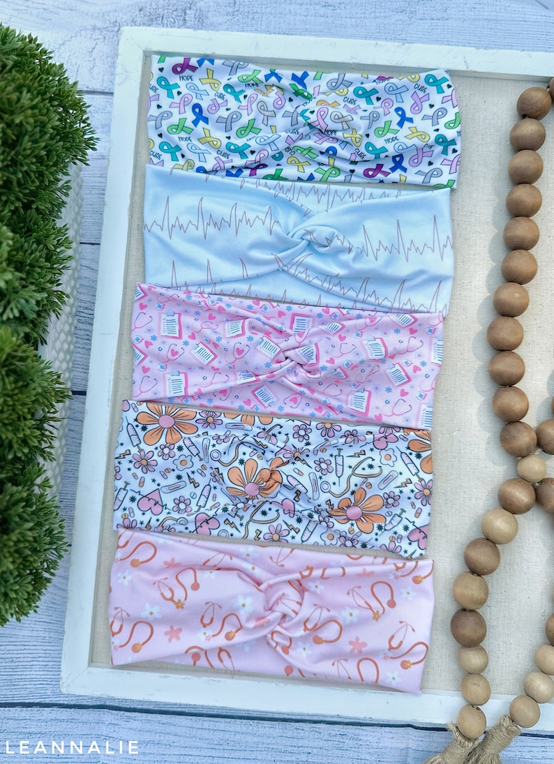 K&ouml;nnte beinhalten: Vier bunte Stirnb&auml;nder mit verschiedenen Mustern. Das obere Stirnband hat einen wei&szlig;en Hintergrund mit rosa, blauen und gr&uuml;nen B&auml;ndern mit den Worten "Hope", "Love" und "Cure". Das zweite Stirnband hat einen hellblauen Hintergrund mit einem wei&szlig;en EKG-Muster. Das dritte Stirnband hat einen rosa Hintergrund mit einem wei&szlig;en Muster aus Stethoskopen, Herzen und Pillen. Das vierte Stirnband hat einen wei&szlig;en Hintergrund mit einem rosa Muster aus Blumen, Stethoskopen und Pillen.