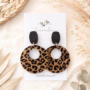 May include: A pair of round leopard print earrings with black wooden tops. The earrings are displayed on a white card with the text "Leannalie.Etsy.com". The earrings have a natural, earthy aesthetic.