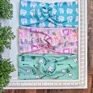 Könnte beinhalten: Drei geknotete Stirnbänder mit Dentalmustern. Eines ist türkis mit lächelnden Zähnen, ein anderes ist rosa mit Dentalwerkzeugen, und das dritte ist mintgrün mit Zähnen, Zahnbürsten und Zahnpasta. Die Stirnbänder sind in einem weißen Rahmen.