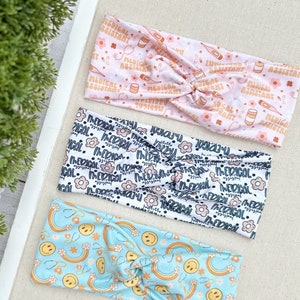 May include: Three colorful headbands with different patterns. The first headband is pink with a white pattern of medical symbols and the text "Medical Assistant". The second headband is white with a black pattern of flowers and the text "Medical Assistant". The third headband is light blue with a yellow pattern of rainbows and smiley faces.