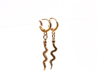 May include: Gold hoop earrings with a dangling snake charm. The snake charm is textured and has a gold finish.