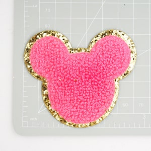 Peut inclure: Oreilles de souris en tissu rose duveteux avec une bordure dor&eacute;e paillet&eacute;e.