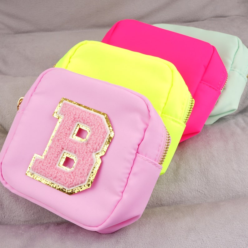 Peut inclure: Trois pochettes zipp&eacute;es en rose, jaune et vert avec une lettre "B" rose et moelleuse sur le devant de la pochette rose.
