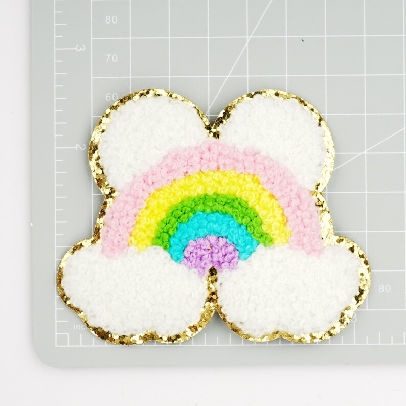 Peut inclure: Un nuage blanc et moelleux avec un arc-en-ciel en tissu pelucheux rose, jaune, vert, bleu et violet. Le nuage et l'arc-en-ciel sont soulign&eacute;s de paillettes dor&eacute;es.