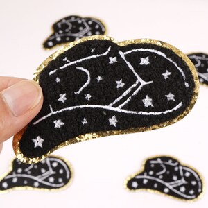 Op de afbeelding: Zwarte viltpatch met een gouden glitterrand en witte geborduurde sterren en een halve maan ontwerp.