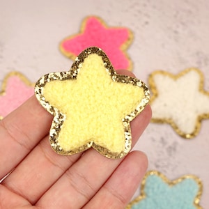 May include: A yellow star-shaped patch with a gold glitter border. The star is made of a soft, fuzzy material.