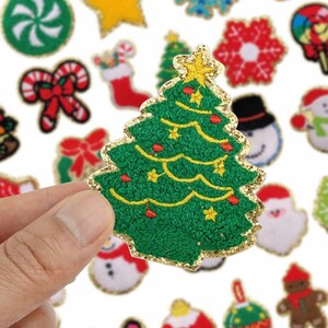 Puede incluir: Un parche de árbol de Navidad verde con borde dorado brillante, una estrella amarilla y adornos rojos. Otros parches festivos incluyen un muñeco de nieve, un bastón de caramelo y un copo de nieve.